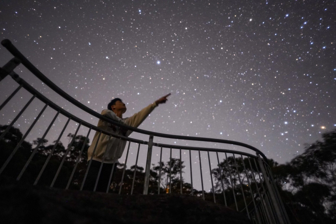 星空の下で階段の手すりに腕を広げる人のシルエット