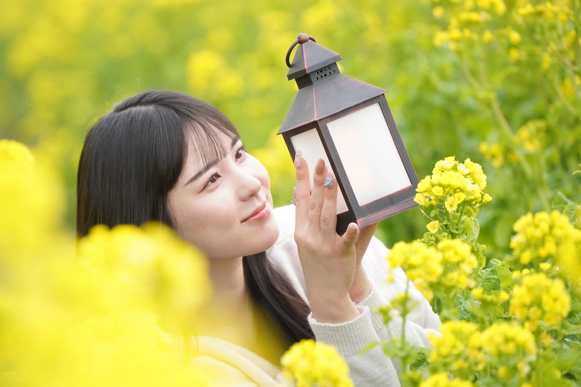 菜の花畑でランタンを持って微笑む女性