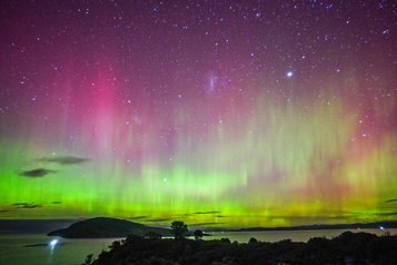 湖の上空に広がるピンクと緑のオーロラと星空